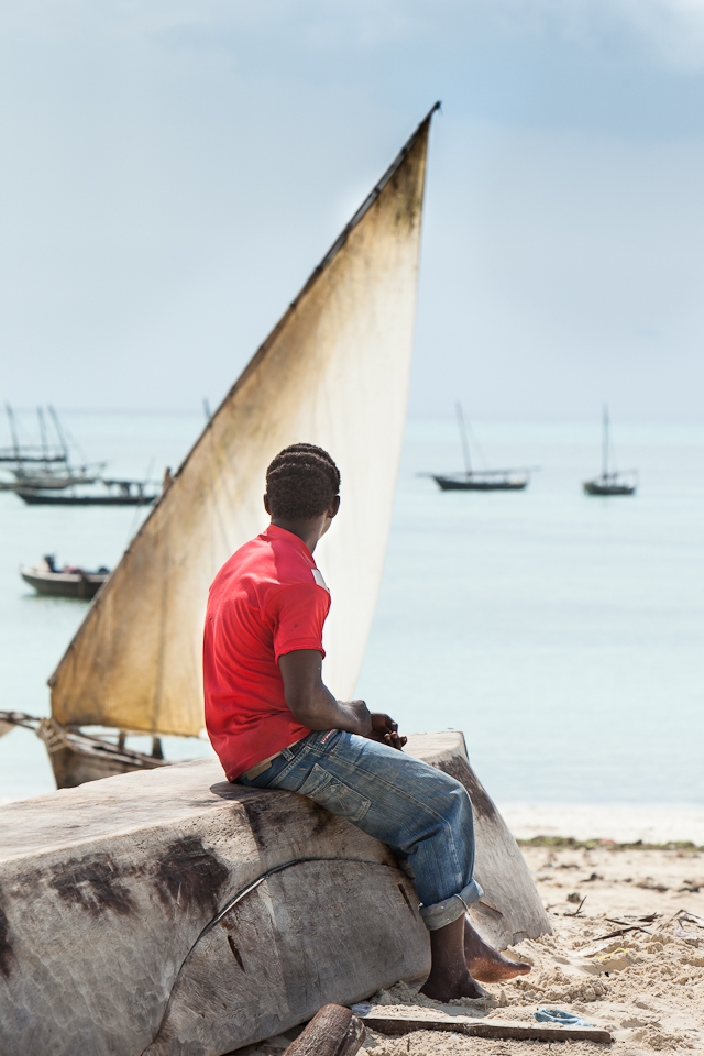 A boy sits on an upturned fishing dhow waiting for the fishermen to return.
