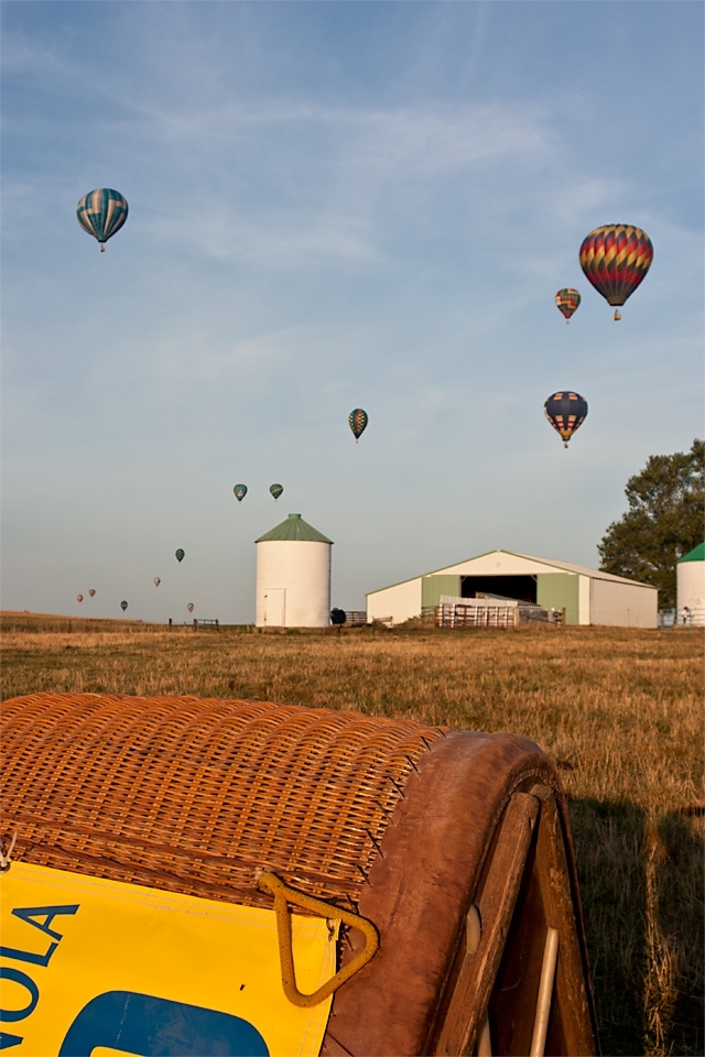 Every year over a hundred hot air balloons compete for ten days at the National Balloon Classic in Indianola, Iowa, USA. A balloon’s basket lies on its side, awaiting launch, while the pilot (shadow on right) watches the other balloons to gauge that morning’s winds.