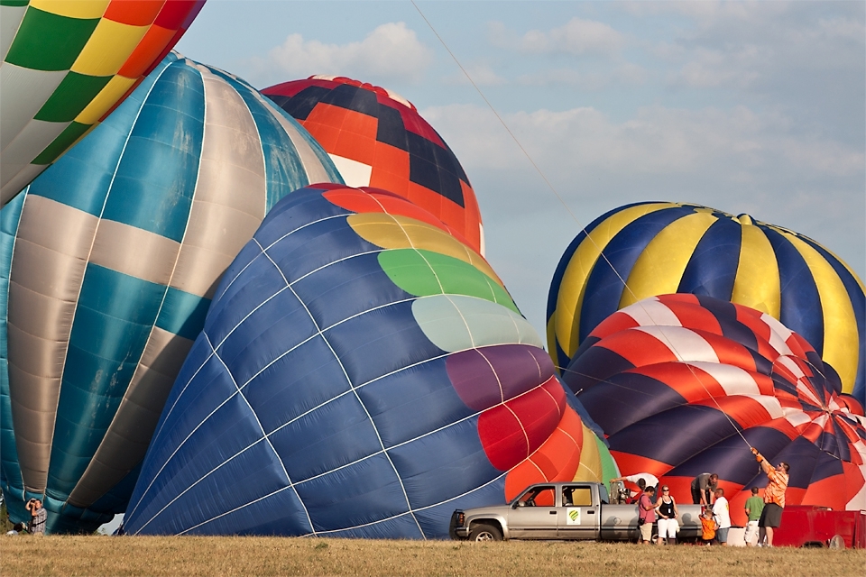 Crews of families and volunteers start inflating hot air balloons for the night glow that starts after sunset.  The man in orange is working the crown line, used to help keep the balloon upright. It can be a real struggle to keep the balloon upright if the winds are too strong.  Indianola, Iowa.