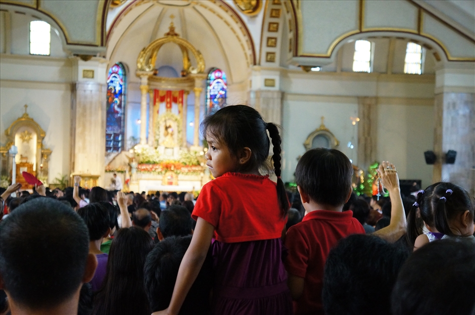 Priests are still highly revered in the Philippines, and are considered the voice of God. Children are hoisted on their fathers' shoulders, along with rosaries, leaflets, and other religious artefacts to receive the final blessing after the mass. Items blessed by priests are believed to improve the lives of their owner. Outside, the market continues to thrive: the merchants struggle to make a few bucks selling superstitous items to unwitting parishioners hoping for a bit of luck.