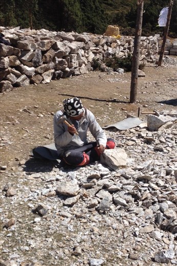 Worker chiseling rock into block. 