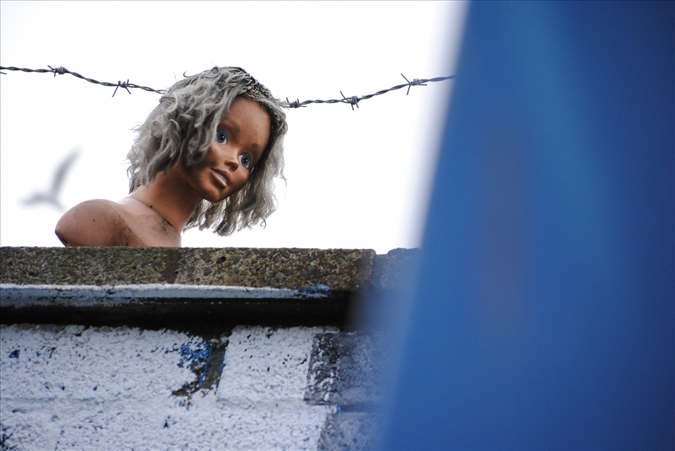 Belfast, Short Strend.
Short Strend is a Catholic enclave in East Belfast, surrounded by the mainly Protestant and unionist neighborhood, from which it is separated by the so called peacewall, a metal barrier 6-7 meters high. Even though many years have passed since the 'Troubles' there objects are thrown from each side to others and sometimes there are aggressions. 
What drove my attention was the connection between the blue eyes of the doll on the peacewall and the blue container. A second later I noticed the barbed wire and the profile of a distant bird.