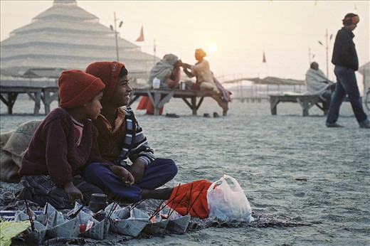 Contrast.
While these boys take delight in the spectacle all around, young men in the background focus inwards, smoking a chillum of Shiva's holy herb before entering a haze-like trance

The whole Sangam flood plain which this festival resides on, is accessible only for a few months of the year. The normal river flow is 15 meters higher, and thus all infrastructure, like the sand, power poles and even the straw pyramid in the background, are all fleeting appearances on this cyclic landscape