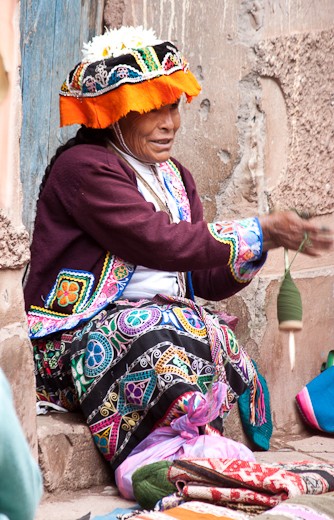 This woman sits in front of her house manually spinning naturally dyed wool which is then used for creating hats, blankets, and other wears.