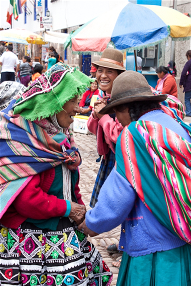 Three local Quechua women stop for a laugh during their market shopping.