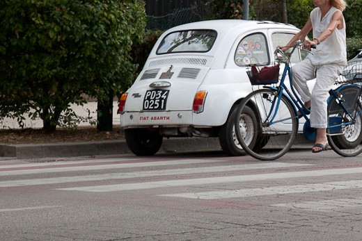 Spirito di Lido: A woman rides her bicycle by a Fiat Abarth in Lido on a hot summer's day.