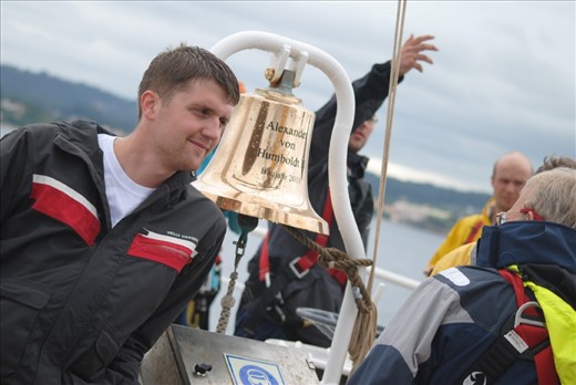 Make ready for to go. The ship's bosun poses beside the main bell on the foredeck as we leave A Coruna. The quiet confidence on his face reflects the mood of the crew who, under a new captain, were ready for success. Another crew member signals instructions behindd him. 