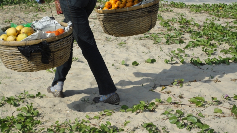 A fruit seller walks the beach trying to sell some fresh fruit in the popular resort of Sanya, an island off the South Coast of China (popular with the new rich Chinese and Russian tourists)
