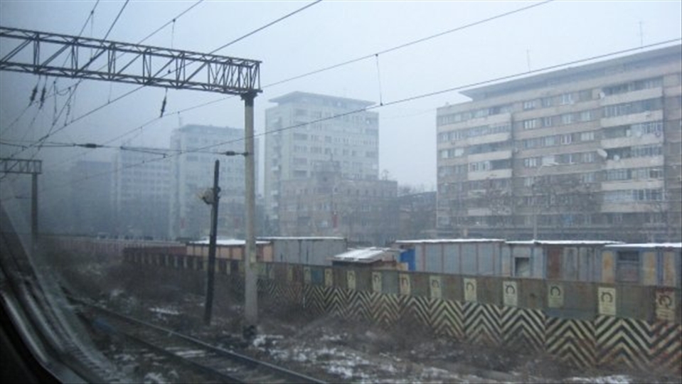 on the train leaving Bucharest North Station you can still see the apartment buildings in the foggy afternoon of a december day