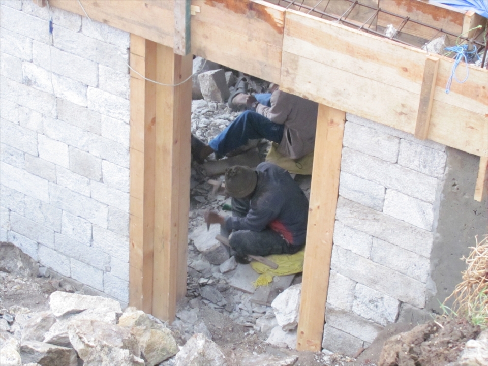 A Nepali craftsman from the lowlands hews blocks of stone by hand for the construction of a new lodge in Namche Bazzar as the demand for more beds increases annually. Notice the perfection of the blocks which have already been laid. 