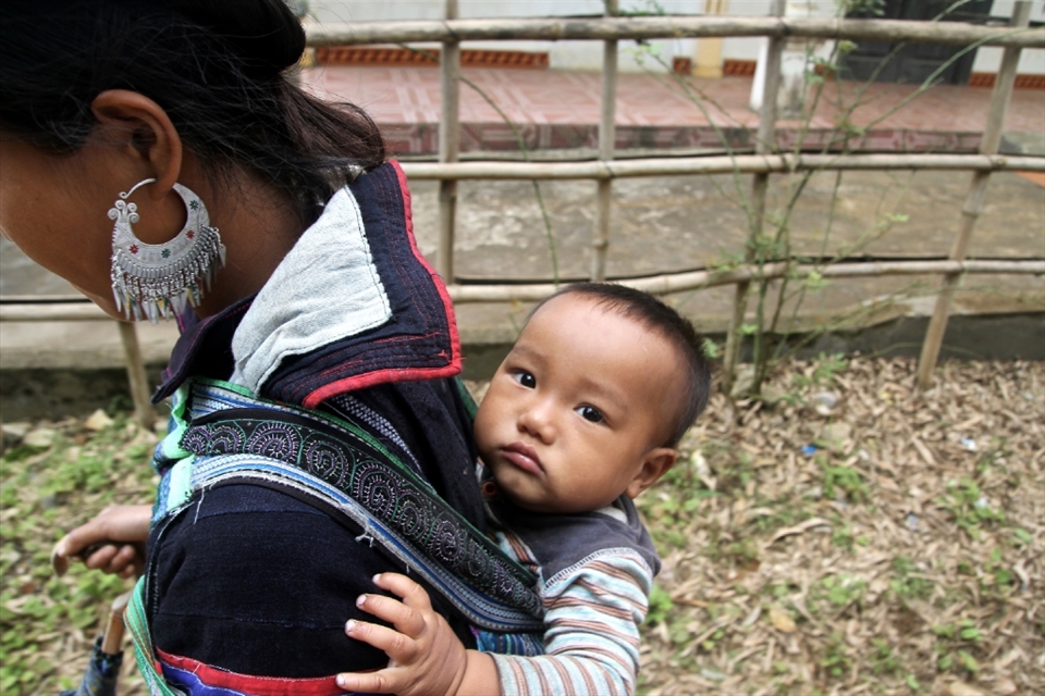 A young member of the Black H'mong tribe in Northern Vietnam looks on as his mother carries him on her back during their daily five hour trek from the town of Sapa to their home village.