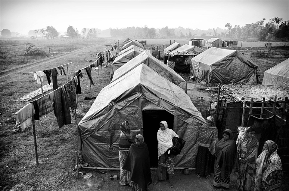 A group of women stand outside one of the tents in the camp. Out of the 600 families, less than one fourth have returned. Vacillating between debris and dreams of what used to be, they battle everyday, rebuilding bamboo by bamboo, towards a bricked structure. They hope for not much, but a house they can live in.