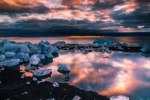 a tidal pool amidst the glacier ice thrown back to shore;  the red and blue sunrise captured in the still water
