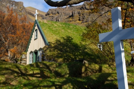 A church ensconced in earth and grass.  the shadow of the tree and the cross in the forground project life and death