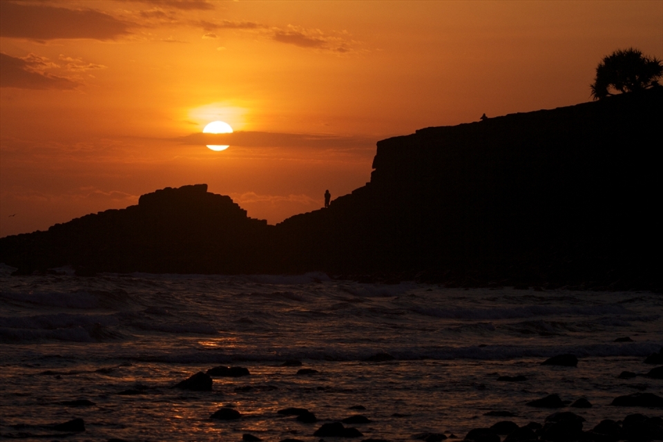 A hot summer sun rises over Fingal headland to bathe the coast in warmth. 