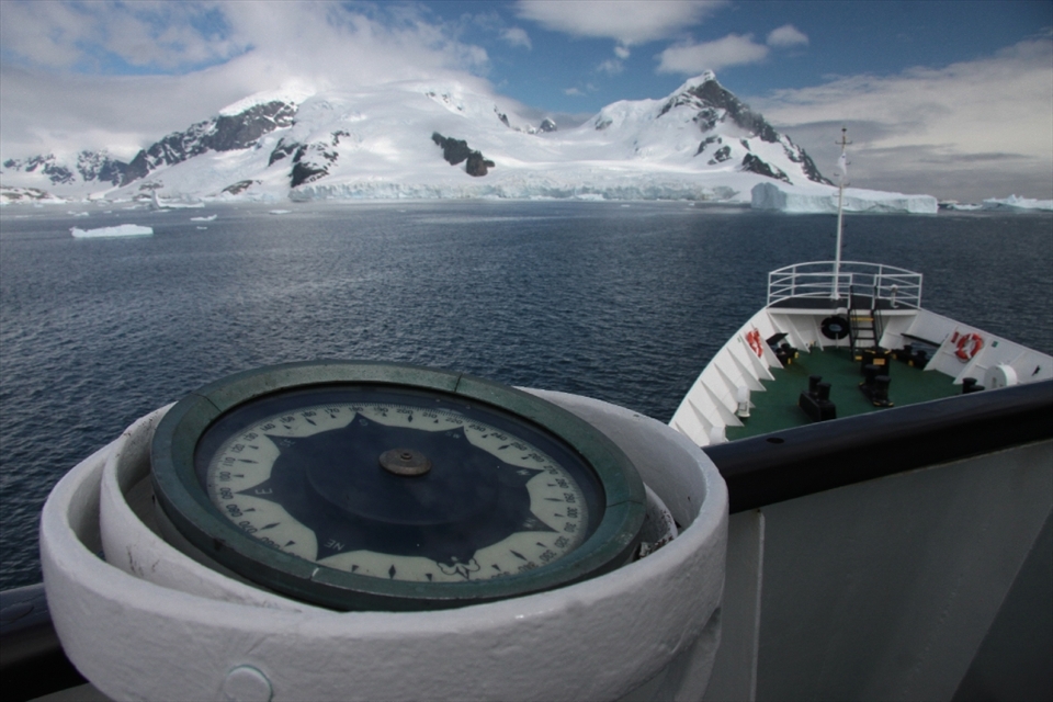 The MV Ushaia's compass points South West as it guides the mighty ship's bow through single and multi-year ice with jagged mountain ranges in the background. Destination - Brown Bluff Strait.