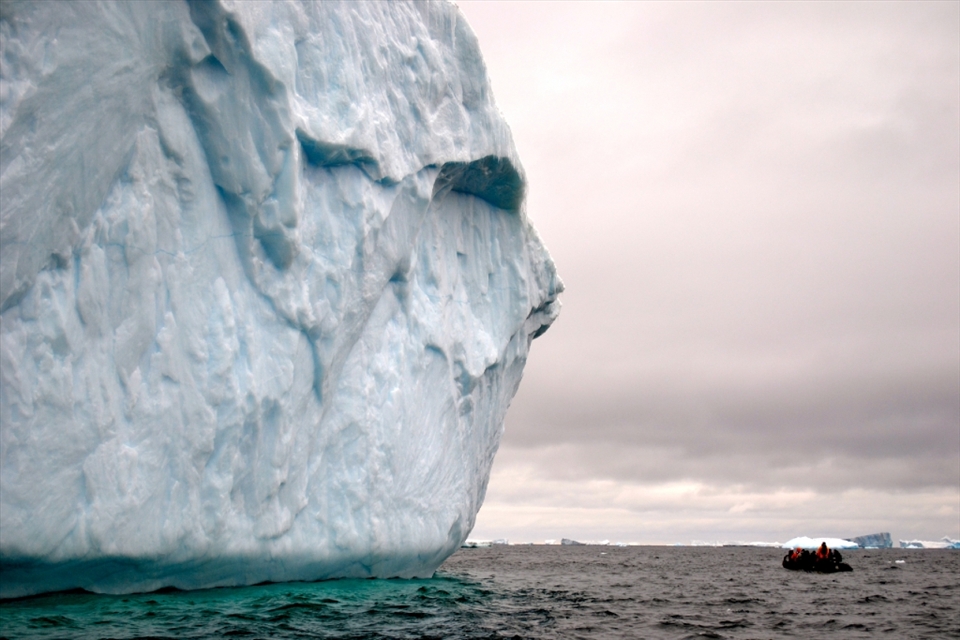 A zodiac of students is dwarfed by an imposing 'face like' iceberg off the coast of Elephant Island, Antarctica.