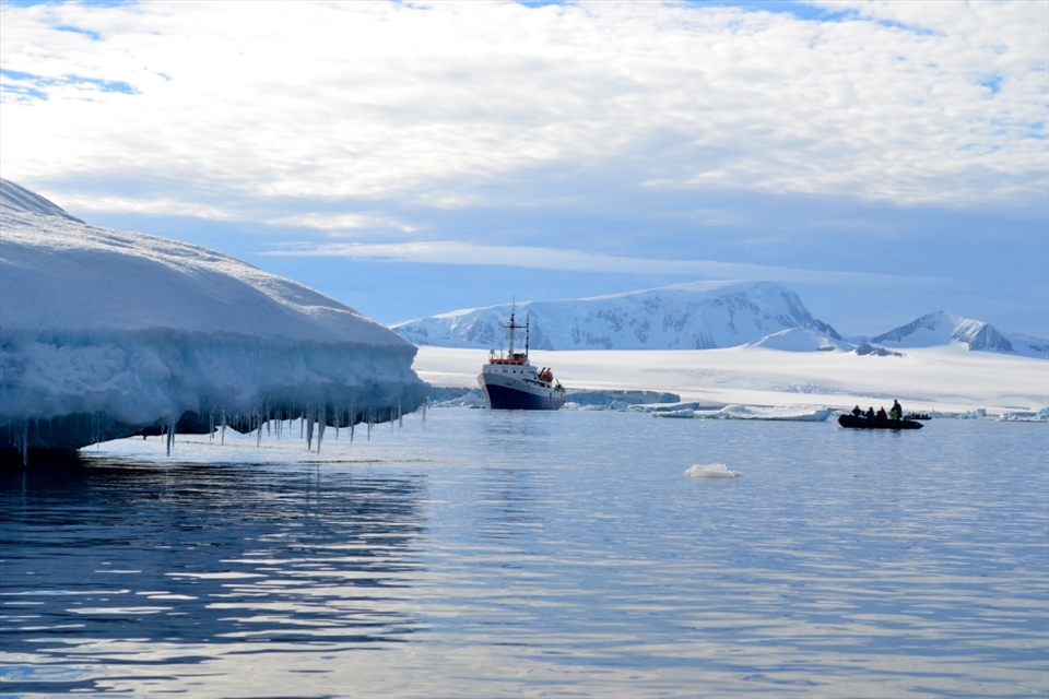 The MV Ushuaia anchors in the Brown Bluff Strait, Antarctica and awaits the return of the zodiacs of exploring students while an iceberg drips fresh water into the sea.