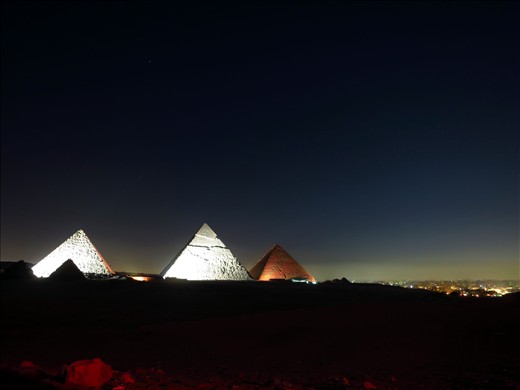 A rare southern view of the Giza Pyramids at night with Cairo lite up.