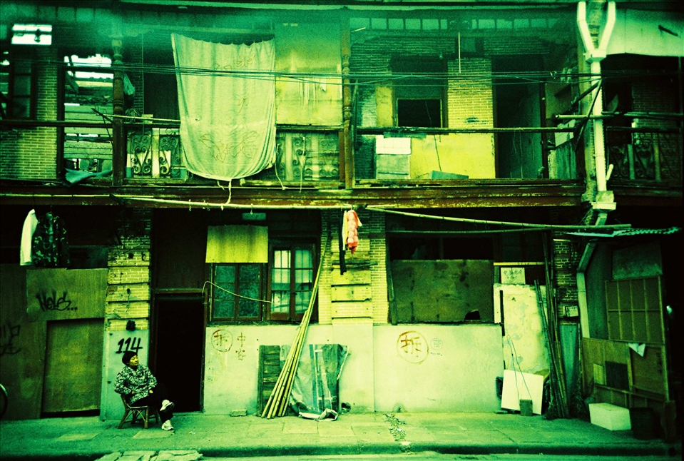 It is common in China for people not to want to leave their soon to be demolished house. This old lady is still living in it. The Chinese character for Demolition is painted on the walls. The urban growth is so high that old must make space for the new despite the protests. Such protests are ignored on behalf that the benefits of the mass are more important than the individual. 
(Analog photo)