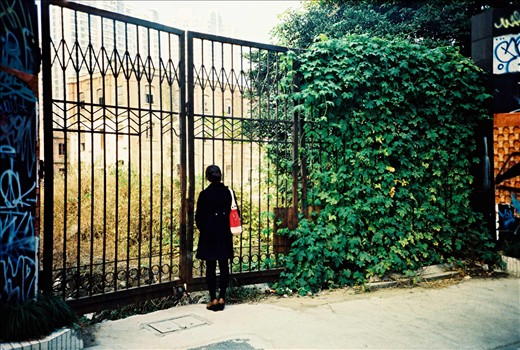 A young girl observing the remaining of an old neighborhood through the gates. She probably never lived in such a neighborhood and is just walking past, ignoring how life could have been before. Like many others she will just walk past and concentrate on the future rather than memories of the past in order to live a 