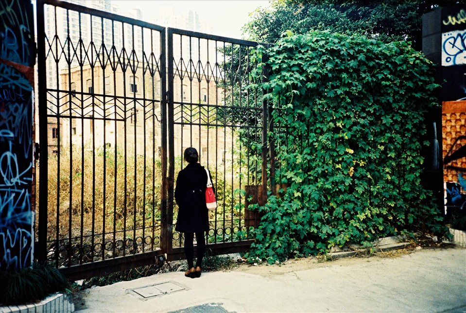 A young girl observing the remaining of an old neighborhood through the gates. She probably never lived in such a neighborhood and is just walking past, ignoring how life could have been before. Like many others she will just walk past and concentrate on the future rather than memories of the past in order to live a 