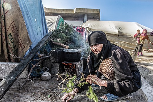 DISPLACED SYRIAN OLD WOMEN COOKING SOUP AROUND A CAMPFIRE IN BAB ALHWA CAMP FOR 