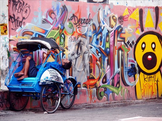 Rickshaw driver resting after hard day at work, on one of quiet streets of Yogyakarta, Indonesia. Many of them spend days and nights on their rickshaws waiting for customers, before returning to their homes, often far from the city.