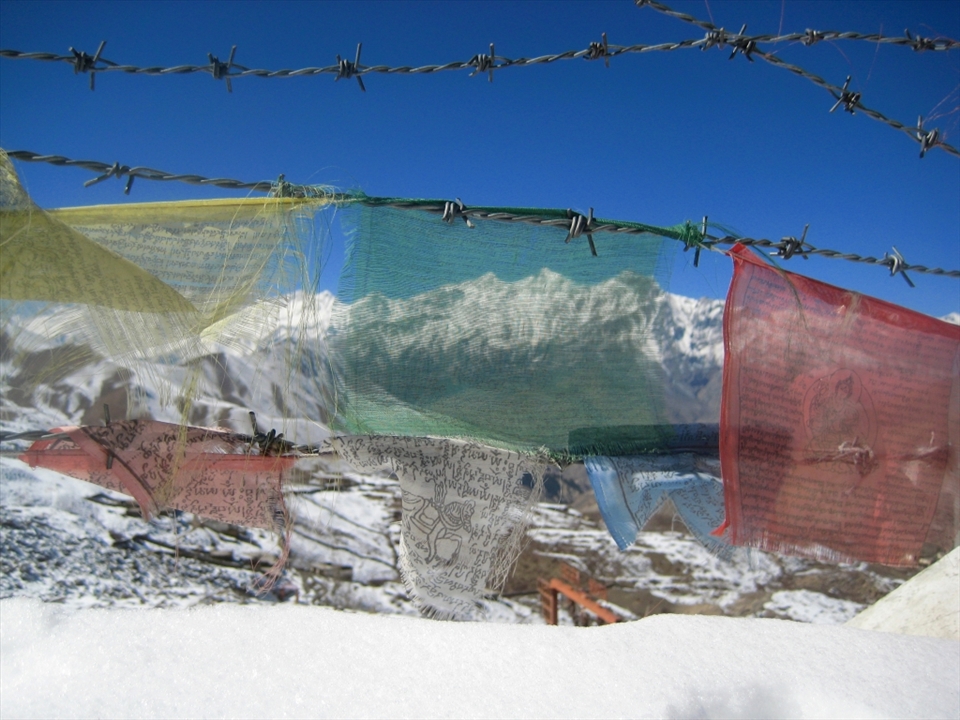 Staring out from a monastery, the Himalaya are framed by snow and barbed wire. The space and silence of the mountains are in stark contrast to the congestion and noise of the city. The prayers of the threadbare flags, weathered by the elements, seem written on the mountains and sky. 