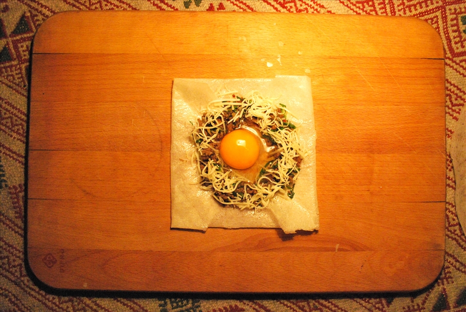 The filling in the middle. Press a well in the filling and place the egg in it. Fold the square to form a triangle. Fry the Brik and serve hot.