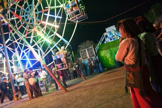 Nuns standing apart look questioningly at the bustle around the hand-operated Ferris wheel. Emblematic of the mutations, youth adopt a new dress style conveyed by TV (satellite dishes are allowed since 2011). Jeans are replacing the traditional longyi. Karaoke clips are now performed by western dressed actors with modern house and ATV.

After decades of oppression, population discovers the consumer society and parents don't want their kids to be deprived as they have been.
