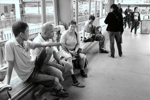Waiting for the next trip, passengers at a jeepney station lull the afternoon away, chatting with each other. Not all stations are equipped with benches, sunshades, and security guards, such as this one. 
