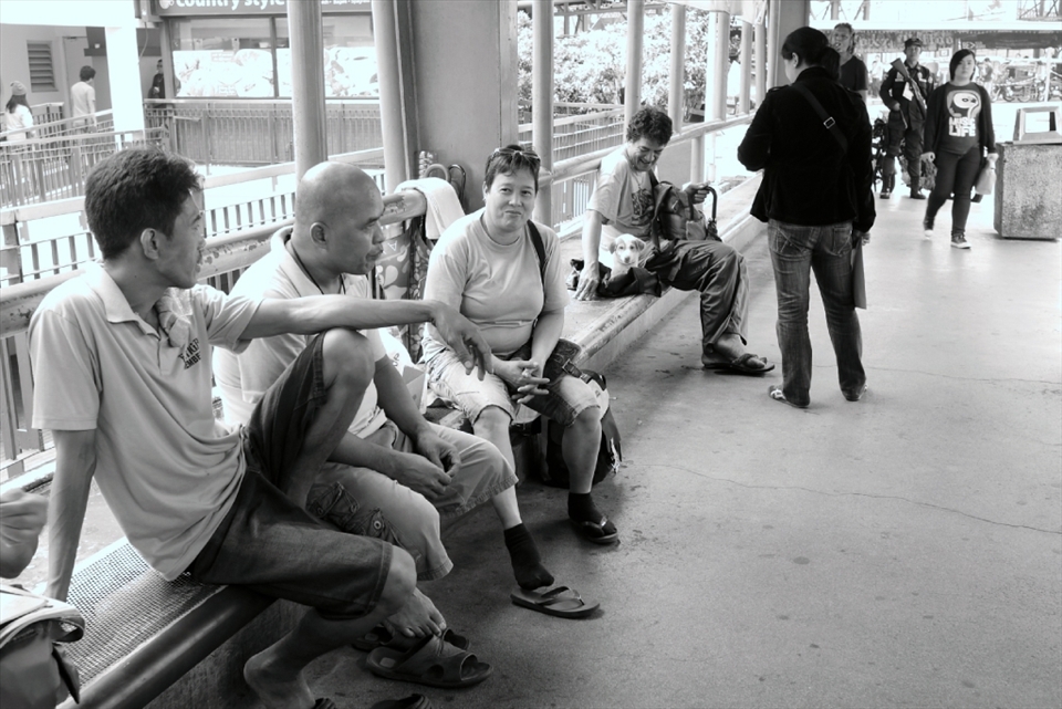 Waiting for the next trip, passengers at a jeepney station lull the afternoon away, chatting with each other. Not all stations are equipped with benches, sunshades, and security guards, such as this one. 