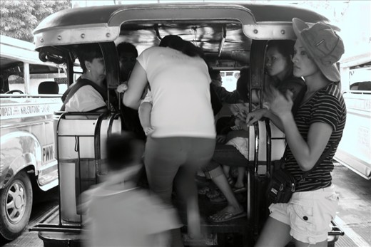 Passengers of all ages climb aboard the jeepney. The woman wearing a hat, standing behind the jeepney doubles as a fare collector and a barker. 
