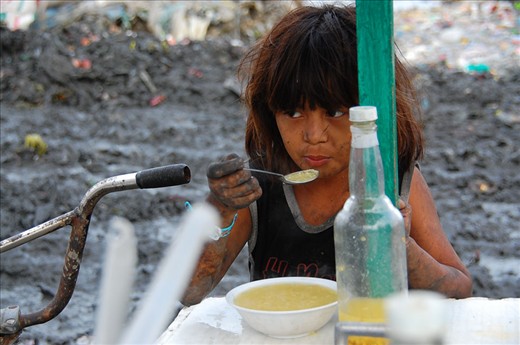A young boy takes a break from working and takes a moment to eat soup. He seemed famished after working for so long that he finished his soup immediately. For most of us, the idea of eating in the middle of a giant mountain of trash might be unthinkable, but he didn’t seem to mind. 
