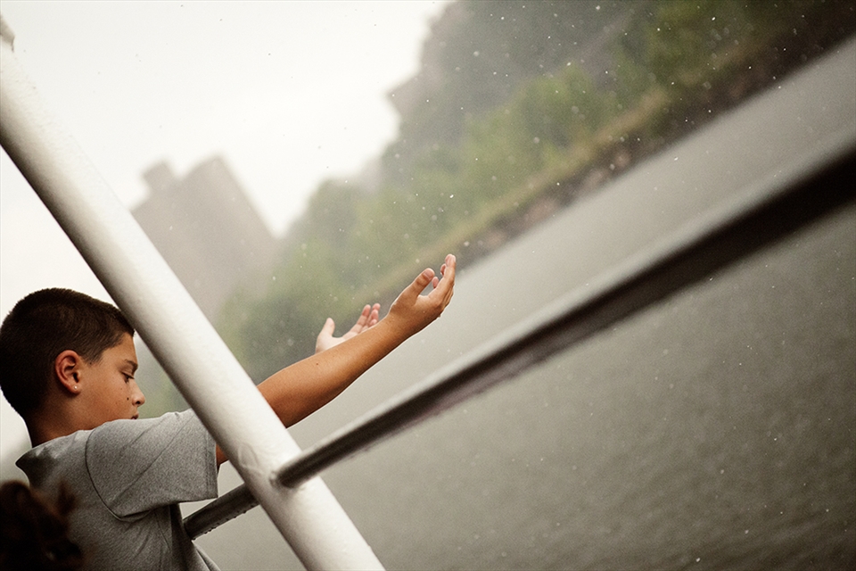 A naive boy. Although it rained, he still enjoyed the trip of river cruise. The rain made the New York fresh.  