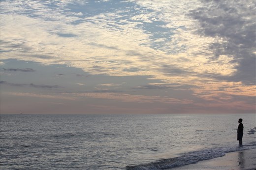 A man looks out at the horizon toward Fort Myers Beach, where condos dot the skyline. Evenings on Sanibel often bring long lines of clouds that absorb the color of the sun as it sets. 