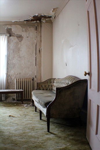 The ghosts of those who might once have sat upon this stately piece of furniture hang thick in the musty, mildewed air of this room. Soft light streaming through sheer curtains has over the years faded the couch's supple velvet to a drab yellowy grey, though hints of a deep slate blue still linger in the cracks of the cushions.