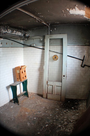 In the basement lie the remains of a labyrinthine men's room. Snaking through an uncomfortable hallway, small rooms reveal themselves: a wide and open wash room, a cluster of narrow shower stalls, an elevated alcove full of urinals, a row of toilets with marble dividers. In the former steam room, a door from a public telephone booth -- a relic from a bygone era -- sits forgotten while chunks of ceiling plaster fall and gather on the tile floor.