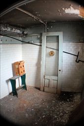 In the basement lie the remains of a labyrinthine men's room. Snaking through an uncomfortable hallway, small rooms reveal themselves: a wide and open wash room, a cluster of narrow shower stalls, an elevated alcove full of urinals, a row of toilets with marble dividers. In the former steam room, a door from a public telephone booth -- a relic from a bygone era -- sits forgotten while chunks of ceiling plaster fall and gather on the tile floor.: by errolume, Views[491]