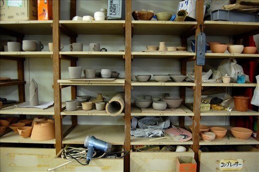 The walls of the room are lined with cluttered pottery of varying stages of completion.