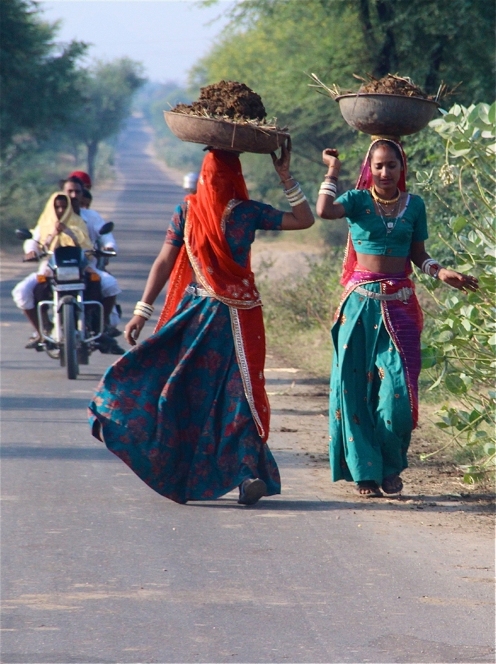Two women carrying cow dung patties used for burning