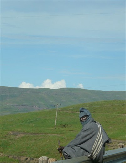 The noise of passersby traveling on the road behind him gets the attention of this lone herder collecting his thoughts. He sits on the metal railing of a meandering highway while watching his herd in the distance as the sun glistens on his face. It is not uncommon for herdsman to cross paths with one another every so often in a country where it is estimated that three quarters of the population live in rural areas, where poverty is prevalent and herding is a necessary way of life for so many.