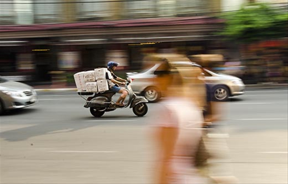 Man goes about his business of delivery on a bike as tourists walk past.
