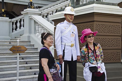 A guard remains unmoving and expressionless as tourists pose with him.