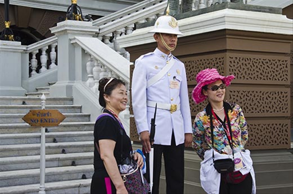 A guard remains unmoving and expressionless as tourists pose with him.