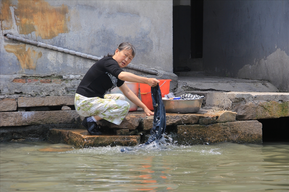 A woman cleans her clothes in outside of her back door in an unsanitary area of the Grand Canal