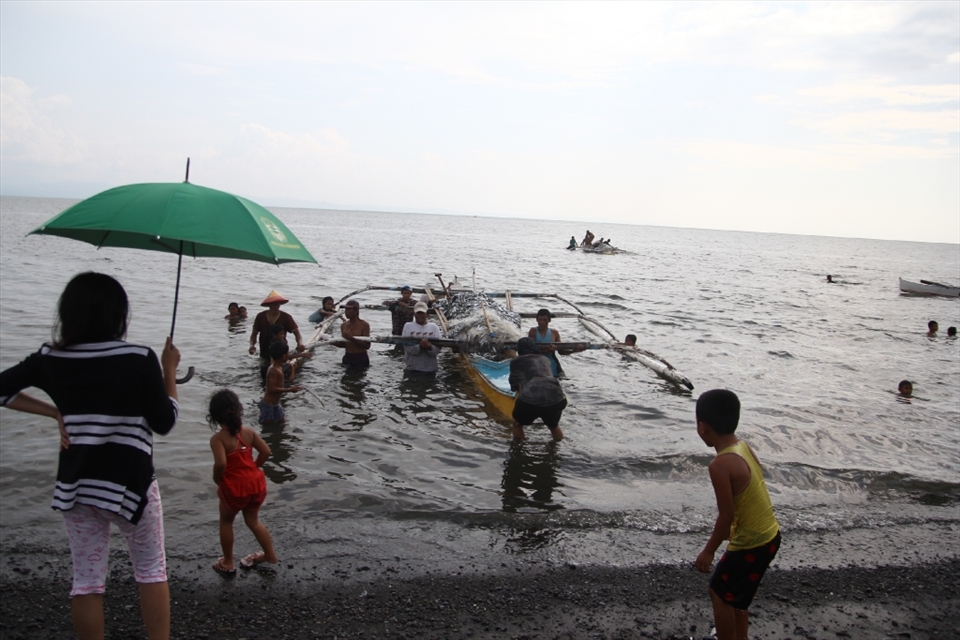 WAITING.  The lady with an umbrella is patiently waiting for the coming boat oozing with sardines. 