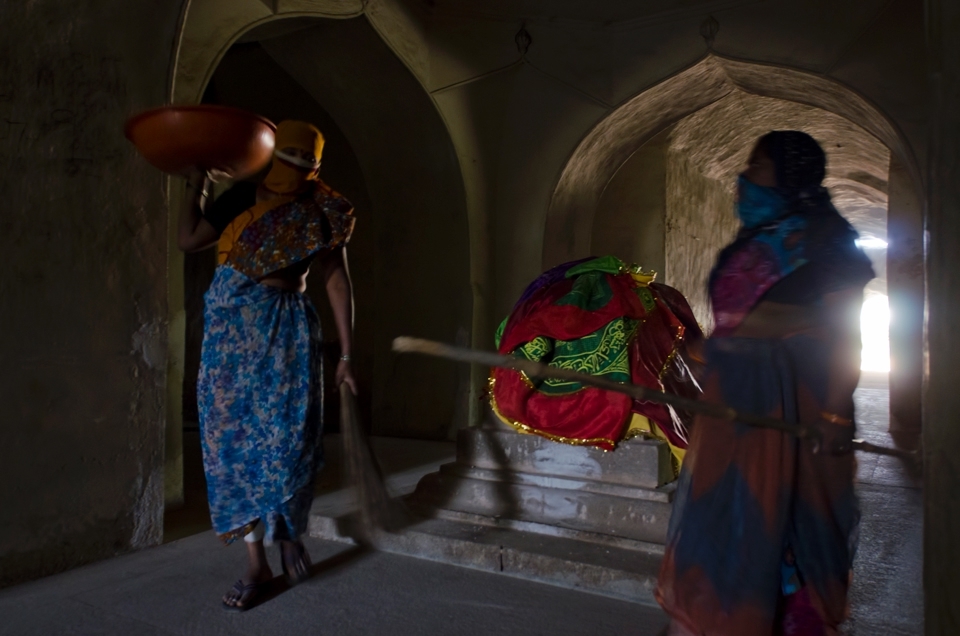 Enter the mausoleum to find a replica of the tomb of Sultan Muhammed Quli Qutub Shah, the fourth king of Quli Qutub Shahi dynasty, built in 1602.
I took a staircase which leads to the base structure supporting the mausoleum. Here, I bumped into the magic of light in these dark galleries and some workers who had finished cleaning the area 
around the actual tomb. The harsh light from the afternoon sun helped the workers in doing their job.