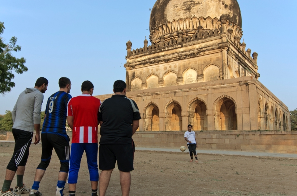 A group of young men playing soccer in the open area around one of the tombs.
